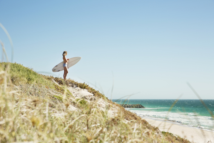 Woman on hill with surfboard looking to the sea